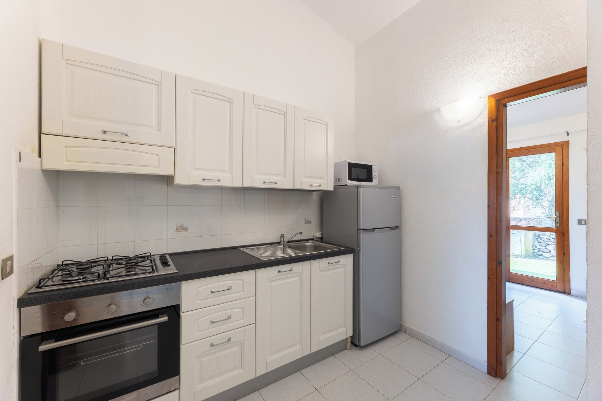 A compact kitchen with white cabinets, a gas stove, an oven, a microwave, and a refrigerator.
