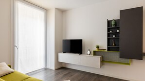 Een moderne woonkamer met een flatscreen televisie op een witte kast, een groene bank en een schuifpui.