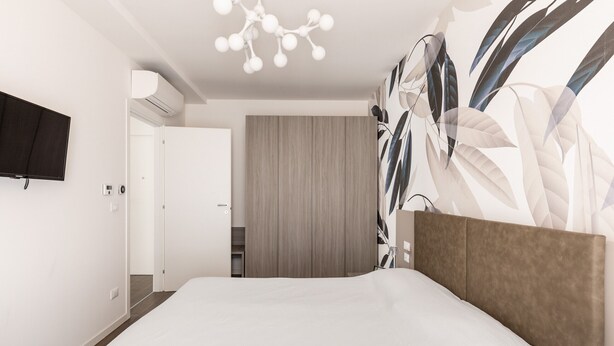 Een moderne hotelkamer met een groot bed, een flatscreen televisie aan de muur en een groot raam met uitzicht op de stad.