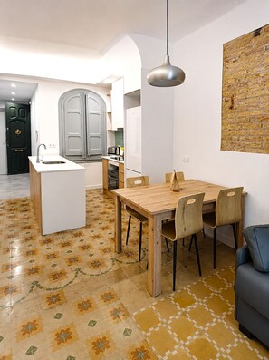 A modern kitchen with a central island, a dining area with a wooden table and chairs, and a living area with a sofa. - LV12 Barcelona Playa Mar-Bella Poblenou (Barcelona)