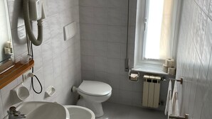 Baño con dos inodoros, un lavamanos, un espejo, un secador de pelo y una ventana.