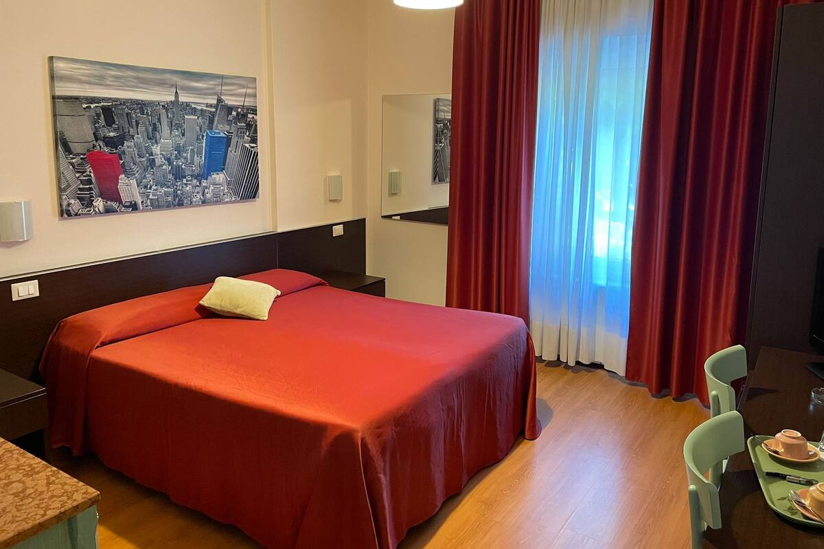 A hotel room with a bed, a dining area, and a cityscape painting on the wall.