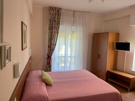 A bedroom with a bed, a wardrobe, a television, and a window with curtains.