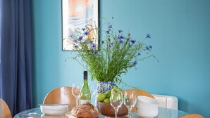 A dining table with a vase of flowers, a bottle of wine, and a bowl of fruit. - Tas Gwynn -  a house that sleeps 4 guests  in 2 bedrooms (St Buryan)