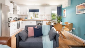 A modern kitchen with white cabinets, a stainless steel refrigerator, and a dining area with a glass table and wooden chairs. - Tas Gwynn -  a house that sleeps 4 guests  in 2 bedrooms (St Buryan)