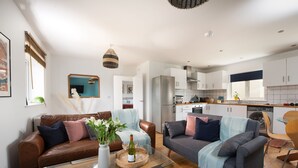 A modern living room with two sofas, a coffee table, and a kitchen in the background. - Tas Gwynn -  a house that sleeps 4 guests  in 2 bedrooms (St Buryan)