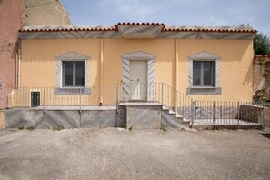 A building with a yellow facade, a tiled roof, and a central entrance with a door. There are two windows on either side of the door, and a small balcony area with a railing. - Casa Bata by Wonderful Italy (Budoni)