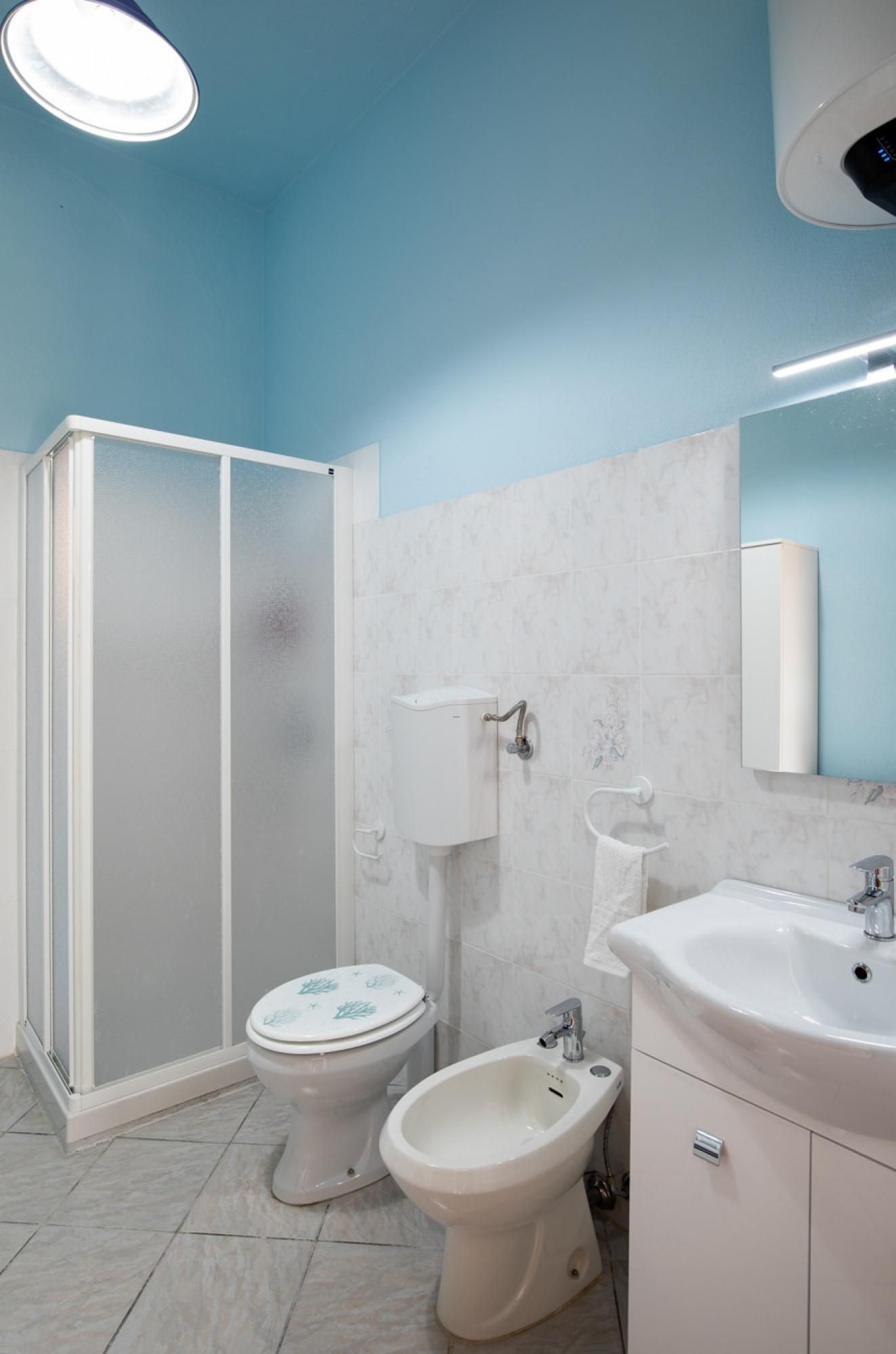 A bathroom with a toilet, bidet, and sink, featuring white fixtures and a blue ceiling.