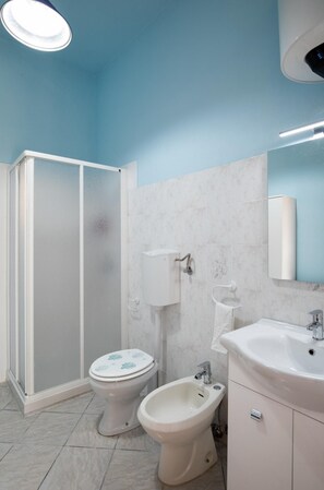 A bathroom with a toilet, bidet, and sink, featuring white fixtures and a blue ceiling.