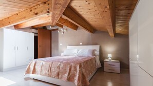 A bedroom with a wooden ceiling, a bed with a patterned bedspread, a bedside table with a lamp, and a wardrobe. - Luna d'Argento by Wonderful Italy - Kimama (Siracusa)