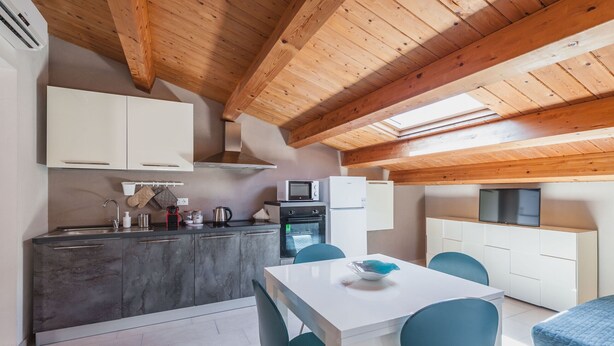 A modern kitchen with a dining area, wooden ceiling beams, and a flat-screen TV. - Luna d'Argento by Wonderful Italy - Kimama (Siracusa)