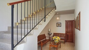 A staircase with a wooden handrail and black balusters, a wooden bench, a table with a vase of flowers, and a door. - Nice Studio on the Terrace (Pozzallo)