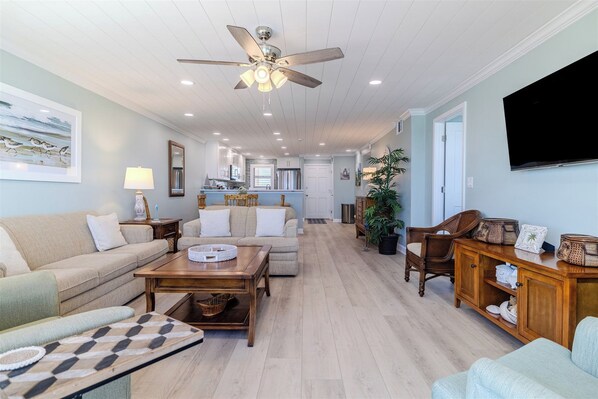 A spacious living room with a ceiling fan, a sofa, a coffee table, and a TV mounted on the wall.
