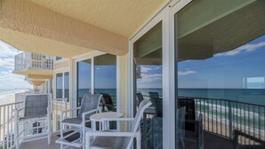 A balcony with white chairs and a table, overlooking a beach and ocean.
