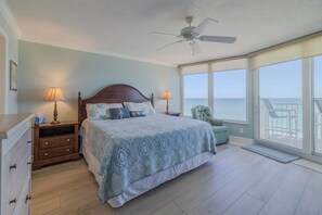 A bedroom with a large bed, two bedside tables, a ceiling fan, and a view of the ocean.
