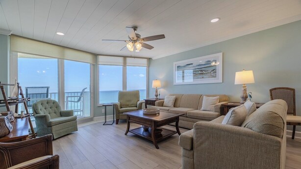 A spacious living room with a view of the ocean, a ceiling fan, and a large window.