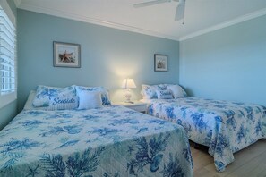 A bedroom with two beds, each with a blue floral bedspread and pillows, a nightstand with a lamp, and framed pictures on the wall.