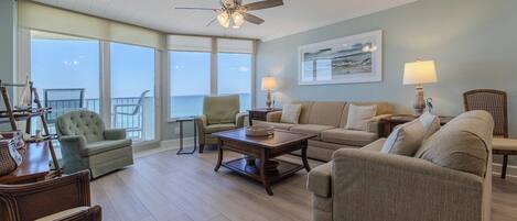 A spacious living room with a view of the ocean, a ceiling fan, and a large window.