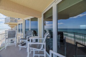 A balcony with white chairs and a table, overlooking a beach and ocean.
