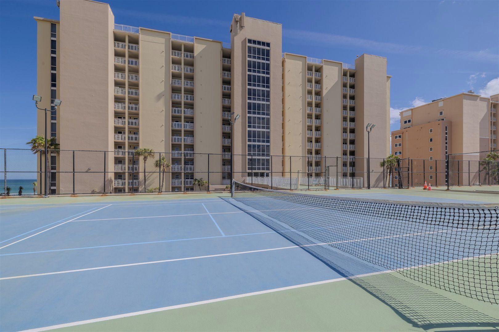 A tennis court with a net in the middle, surrounded by a fence, and buildings in the background.