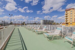 A rooftop deck with sun loungers, a green floor, and a view of a building in the background.