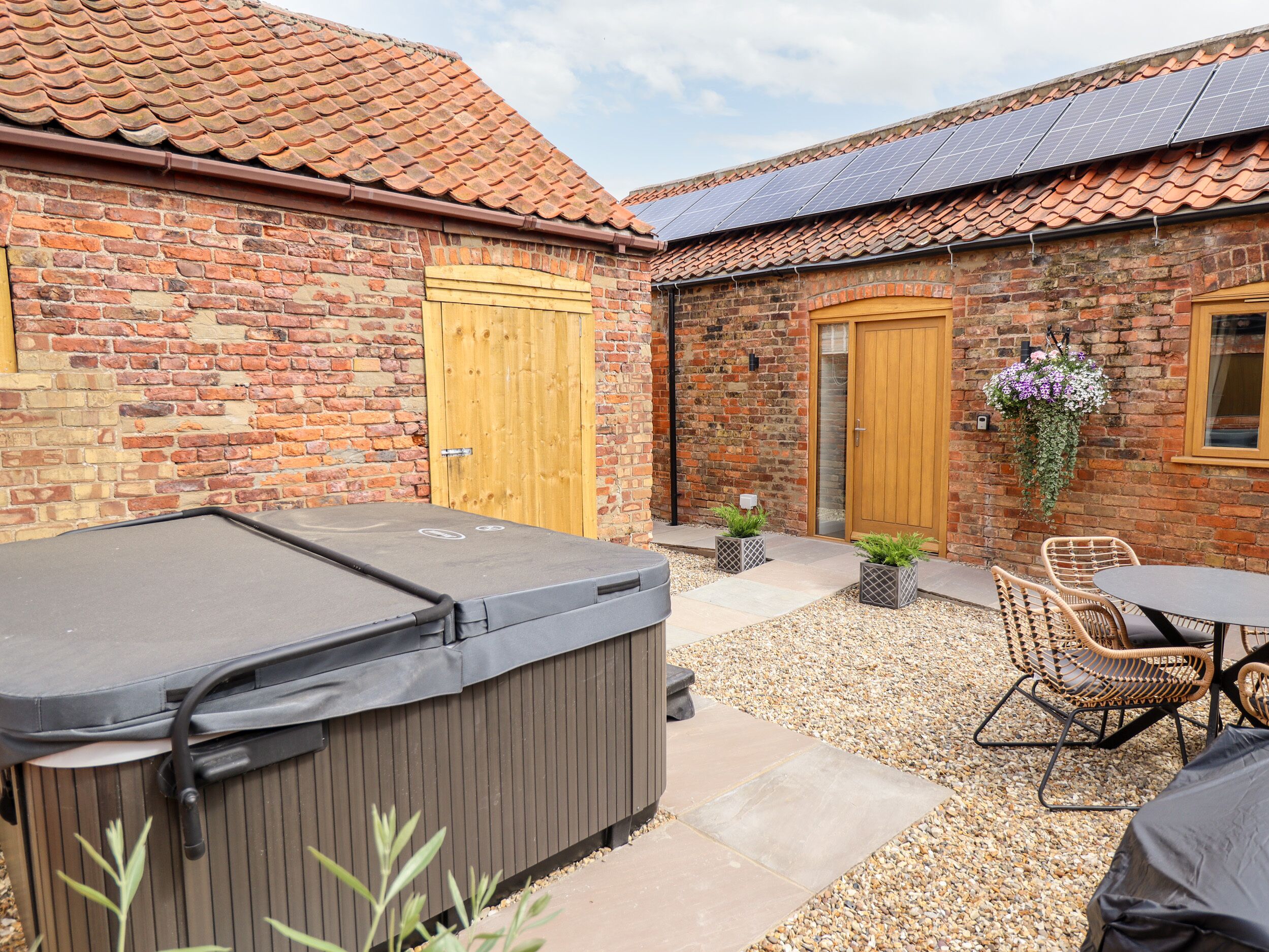 A patio area with a hot tub, outdoor seating, and a brick building with wooden doors.