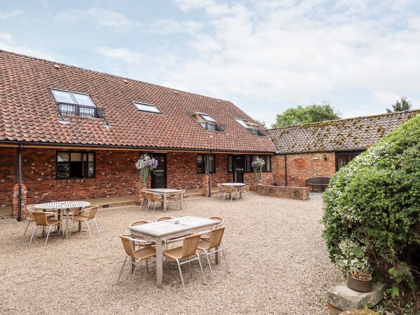 A brick building with a tiled roof, outdoor seating area with tables and chairs, and a gravel ground.