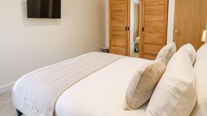 A bedroom with a bed, a TV mounted on the wall, and wooden wardrobes. - The Grange Cottage 1 (Grimsby)