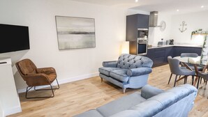 A modern living room with a grey sofa, a brown leather chair, and a flat-screen TV mounted on the wall. - The Grange Cottage 1 (Grimsby)