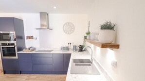 A modern kitchen with a central island, built-in oven, and stainless steel appliances. - The Grange Cottage 1 (Grimsby)