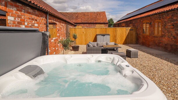 A hot tub in a courtyard with brick buildings and wooden fencing. - The Grange Cottage 1 (Grimsby)