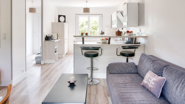 A modern living room with a grey sofa, a small table, and a kitchen area in the background.