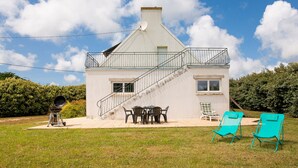 A white house with a balcony, a barbecue grill, and two turquoise lawn chairs.