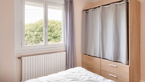 A bedroom with a bed, a window with curtains, a radiator, and a wardrobe.
