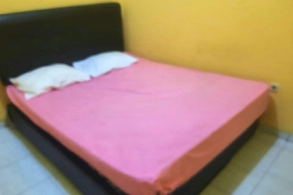 Un lit avec une tête de lit noire et une couvre-lit rose, dans une pièce aux murs jaunes.