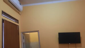 Ein Badezimmer mit Toilette, Waschbecken, Spiegel, einer Tür und einem an der Wand befestigten Fernseher.