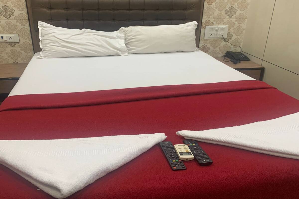 Een hotelkamer met een bed, een rode deken, twee witte handdoeken en drie afstandsbedieningen op het bed.