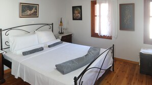 A bedroom with a wooden ceiling, a bed with white linens, a nightstand, a lamp, and a window with curtains. - Angelina's House (Rethymno)