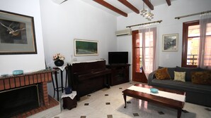 A living room with a fireplace, a sofa, a television, and a piano. - Angelina's House (Rethymno)