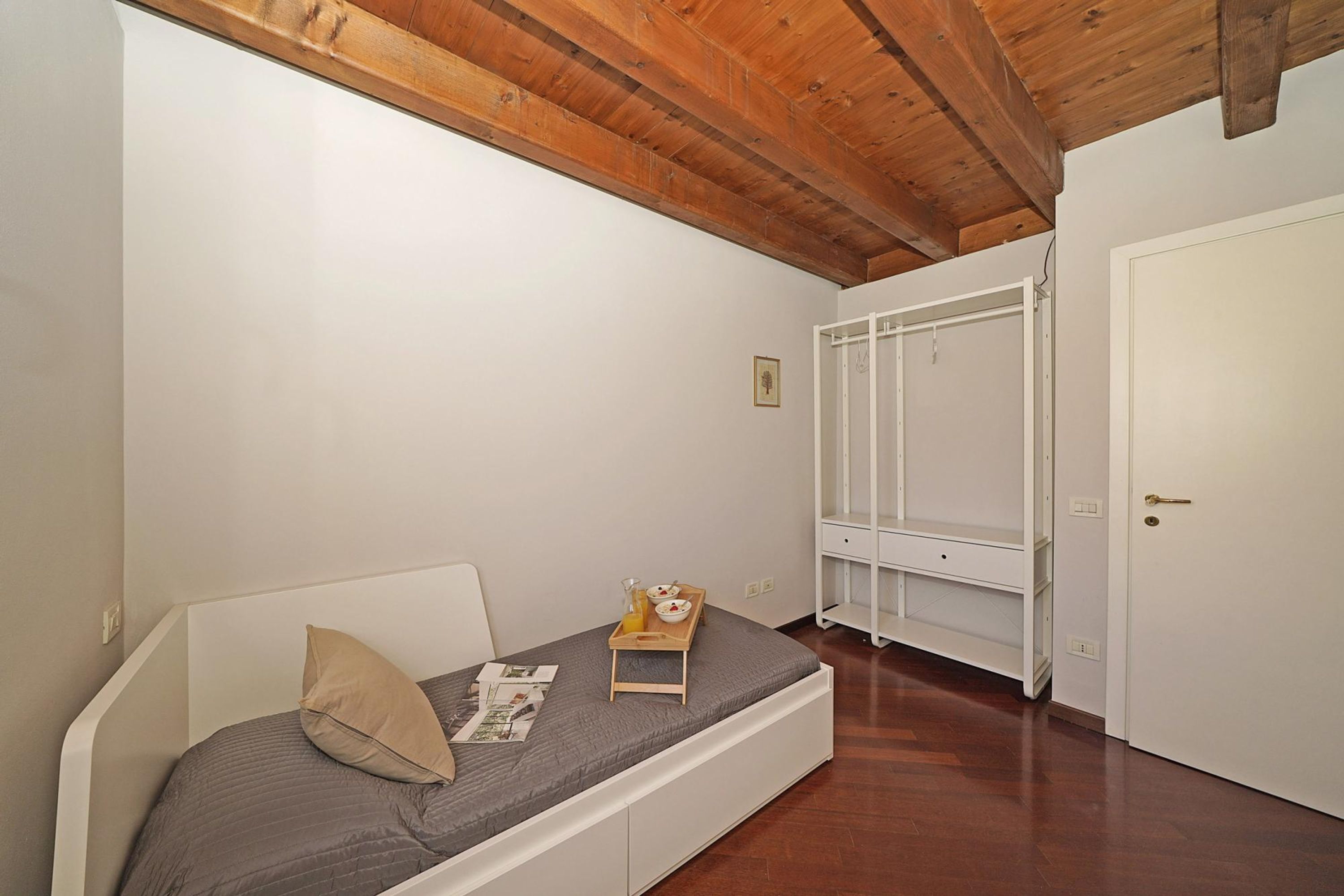 Ein kleines Schlafzimmer mit einem Bett, einer Holzbalkendecke, einem weißen Kleiderschrank und einer weißen Tür.