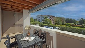 Uma varanda com teto de madeira, uma mesa com cadeiras e vista para uma área residencial com edifícios e carros estacionados.