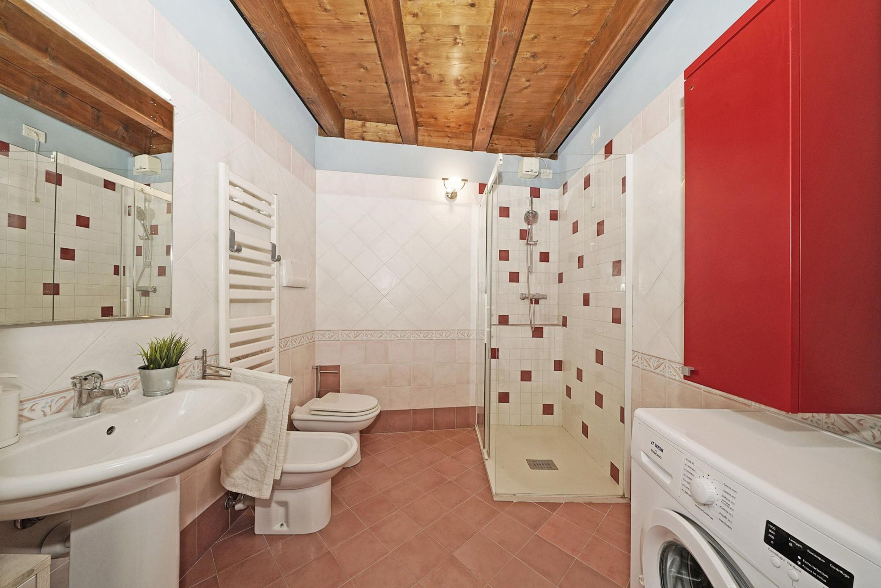 A bathroom with a sink, two toilets, a shower, and a washing machine.