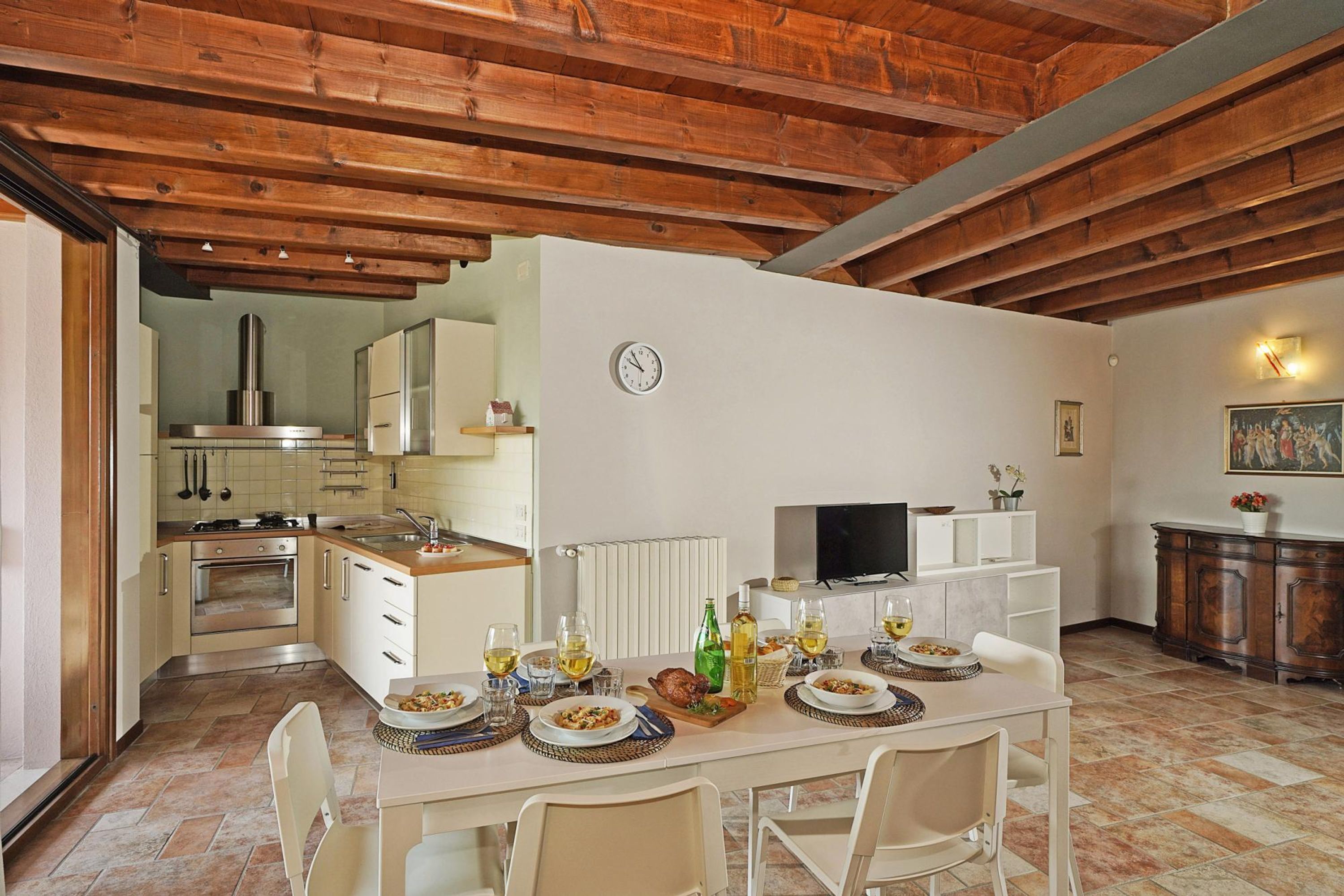 A spacious kitchen with wooden beams, a dining area with a table set for four, and a television on a stand.