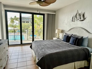 A hotel room with a large bed, a balcony with a view of a swimming pool, and a decorative wall piece. - Stunning Ocean View 2BR/2BA Condo in Exclusive 1800 Atlantic Community (Key West)
