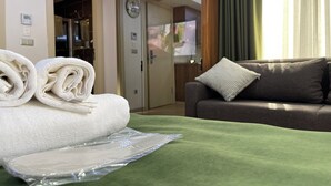 Una habitación de hotel con cama, colcha verde, sofá marrón y un cojín, además de un reloj de pared.