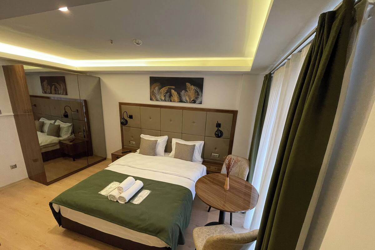 A hotel room with a large bed, a bedside table, a chair, a small round table, and a mirror.