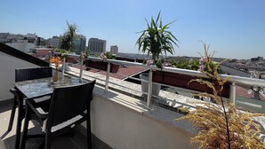 Una terraza en la azotea con mesa y sillas, plantas en macetas y vistas a la ciudad.