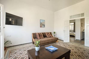 A living room with a sofa, a coffee table, a potted plant, and a painting on the wall. - Vintage Charm 1BR Apt w Balcony & View (Haifa)