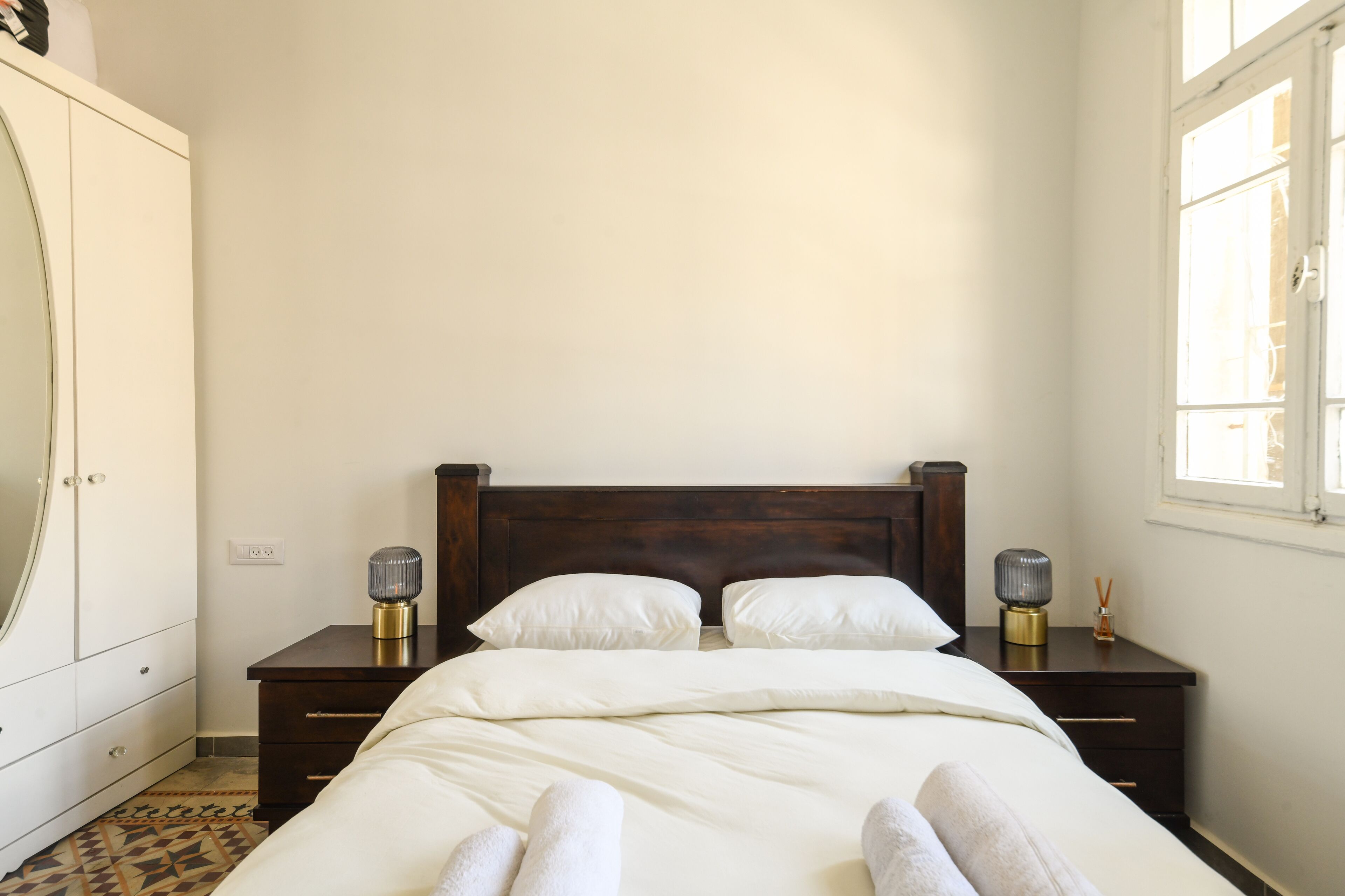 Een keurig opgemaakt bed met witte lakens en twee bedlampjes.