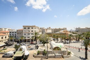 A cityscape with a mix of modern and traditional buildings, a central open plaza with palm trees, and a clear blue sky. - Vintage Charm 1BR Apt w Balcony & View (Haifa)